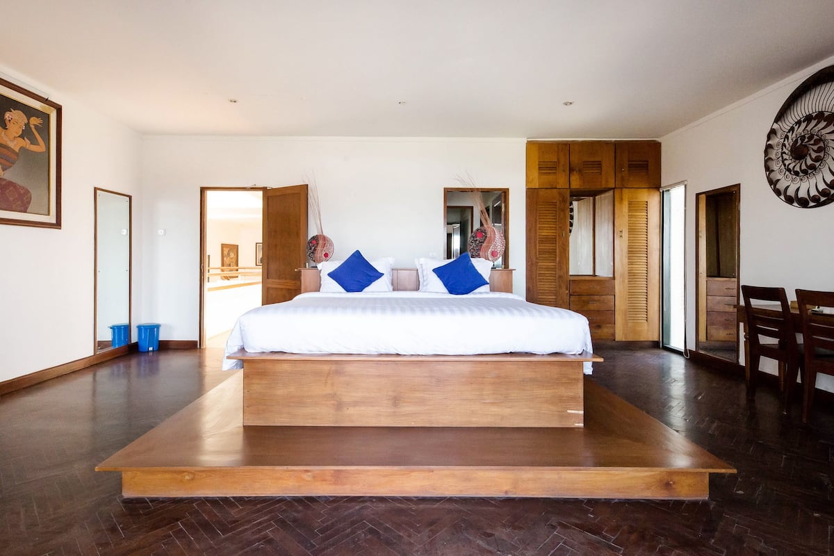 A spacious bedroom with a large bed, wooden flooring, and a view of the outdoors.