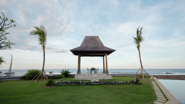 Um gazebo com vista para o oceano, cercado por palmeiras e uma piscina.