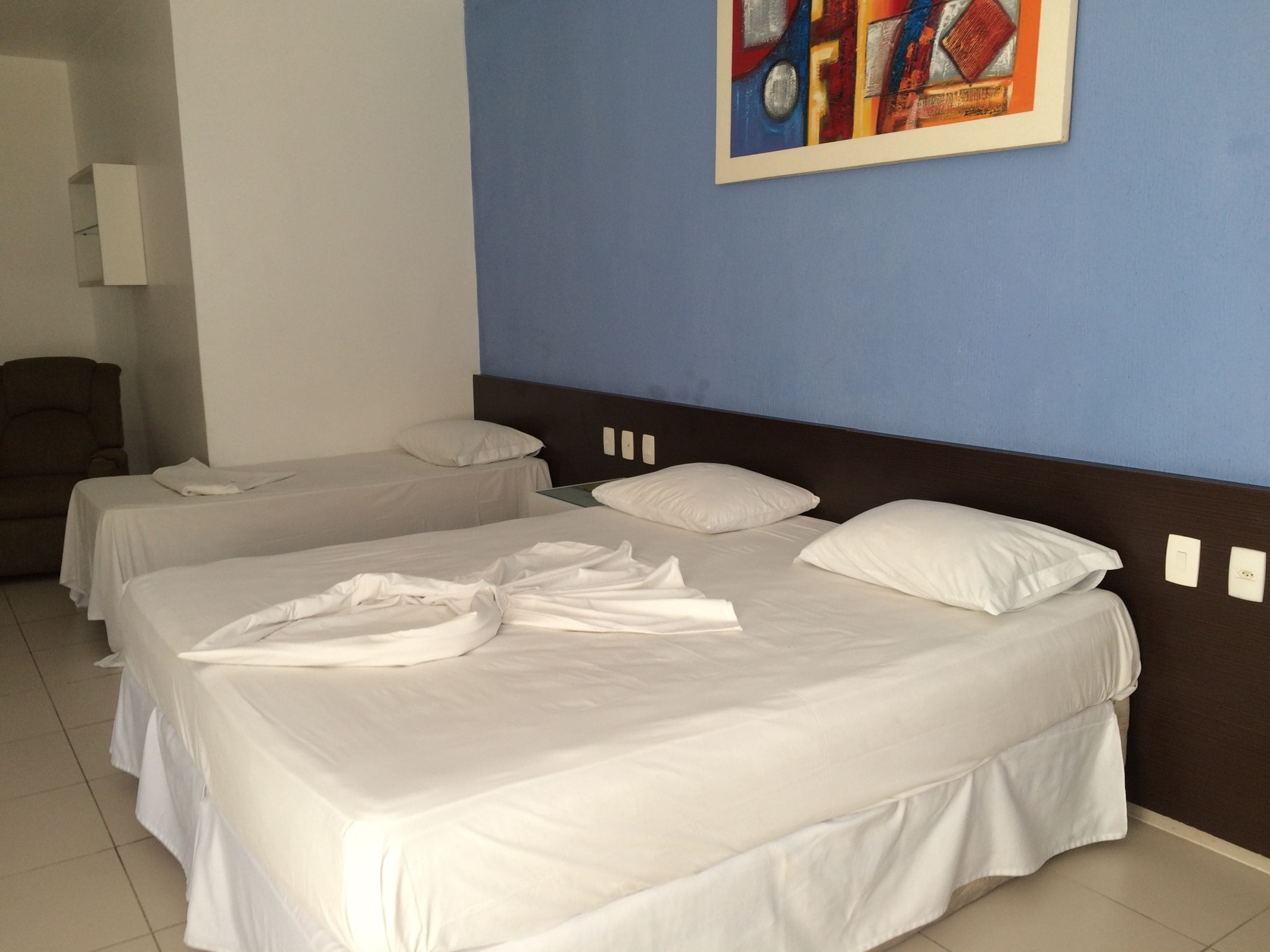 A hotel room with two beds, a brown chair, and a painting on the wall.