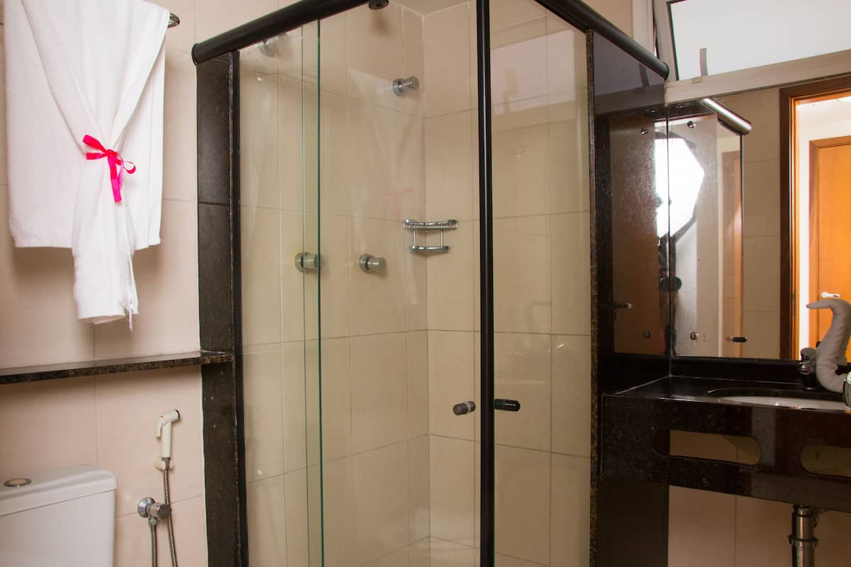 A glass-enclosed shower with a black frame, a white robe with a pink ribbon, and a black sink with a mirror above it.