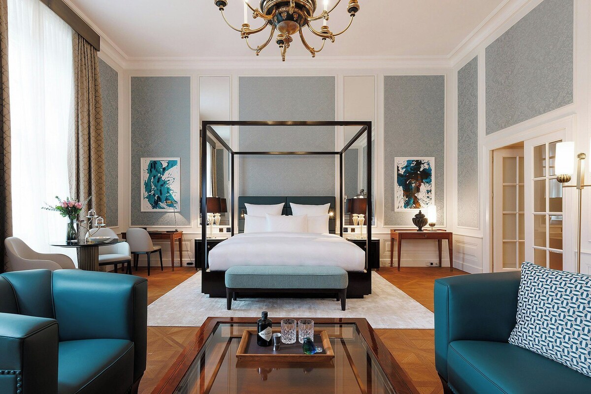 A spacious bedroom with a four-poster bed, a sitting area with a sofa and armchairs, and a dining area with a table and chairs.