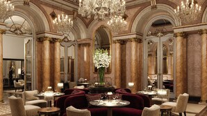 Un comedor lujoso con candelabros ornamentados, columnas de mármol y asientos mullidos.