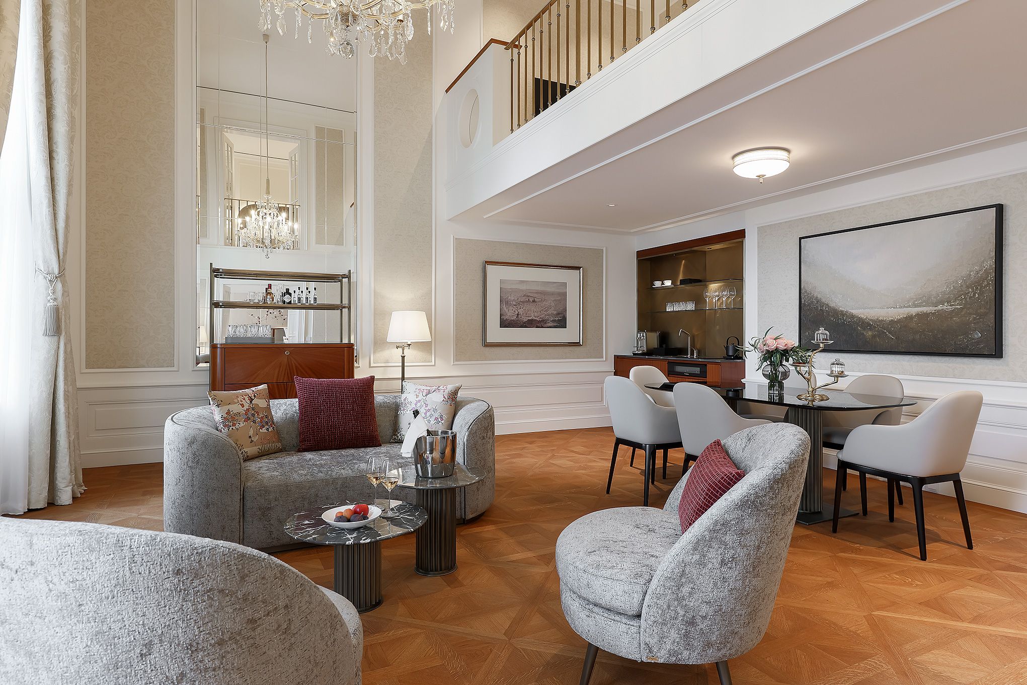 A spacious living area with a high ceiling, a chandelier, a dining table with chairs, and a view of the upper floor.