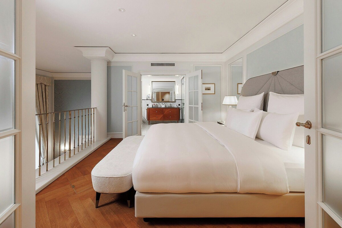 A hotel room with a large bed, a wooden dresser, a mirror, and a balcony with a railing.