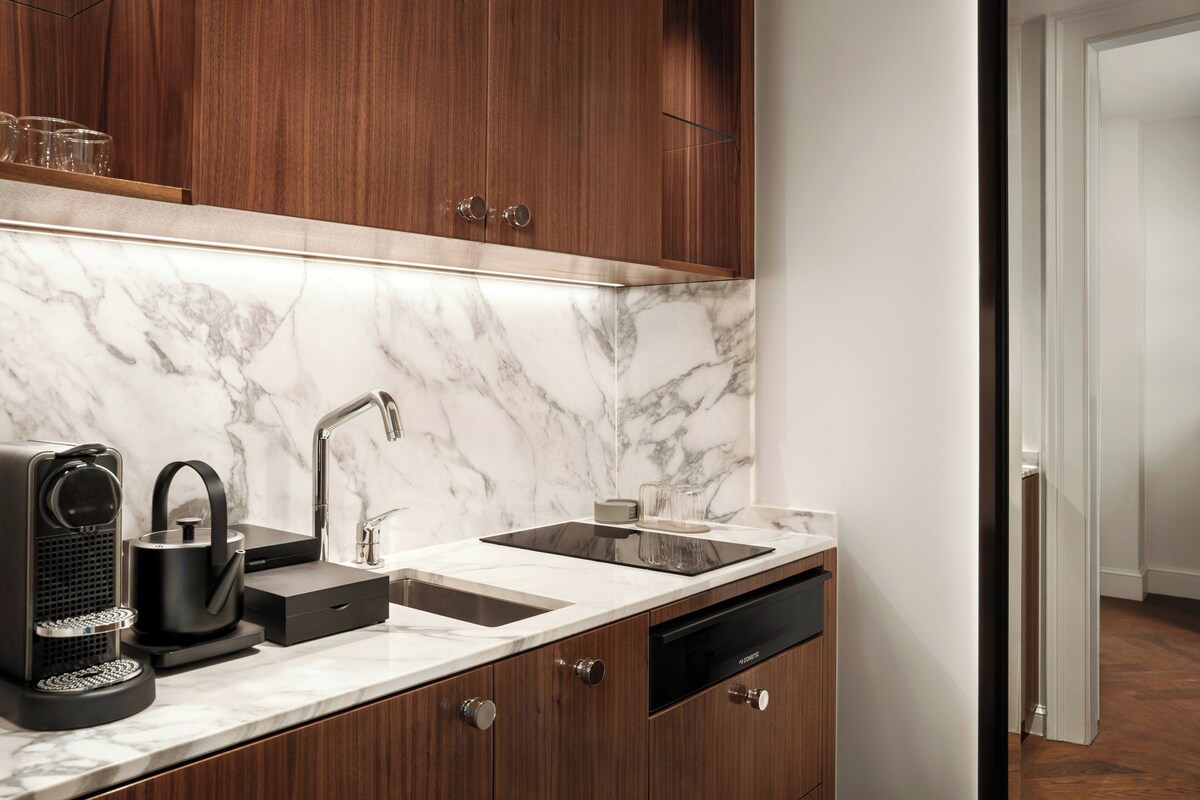 A modern kitchen with marble countertops, a built-in sink, a coffee machine, and wooden cabinets.