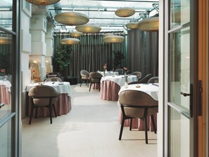 A restaurant with tables set for dining, hanging wicker lamps, and a view through a glass door. - Palais Coburg (Vienna)