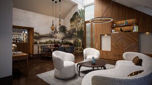 A modern living room with a high ceiling, wooden paneling, and a mural of a tropical landscape. There are two white armchairs, a coffee table, and a dining area with a wooden table and chairs. - Palais Coburg  (Vienna)