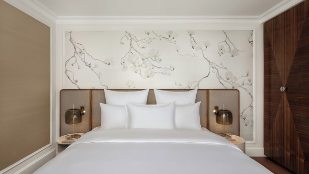 A neatly made bed with white linens, two bedside tables with lamps, and a wall with a floral pattern. - Palais Coburg  (Vienna)