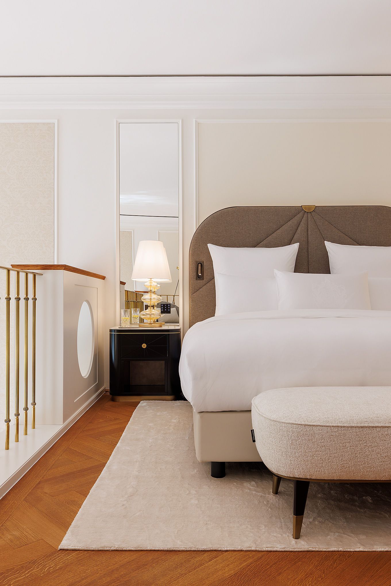 Een hotelkamer met een bed, een nachtkastje, een lamp, een spiegel, een houten vloer en een witte muur.