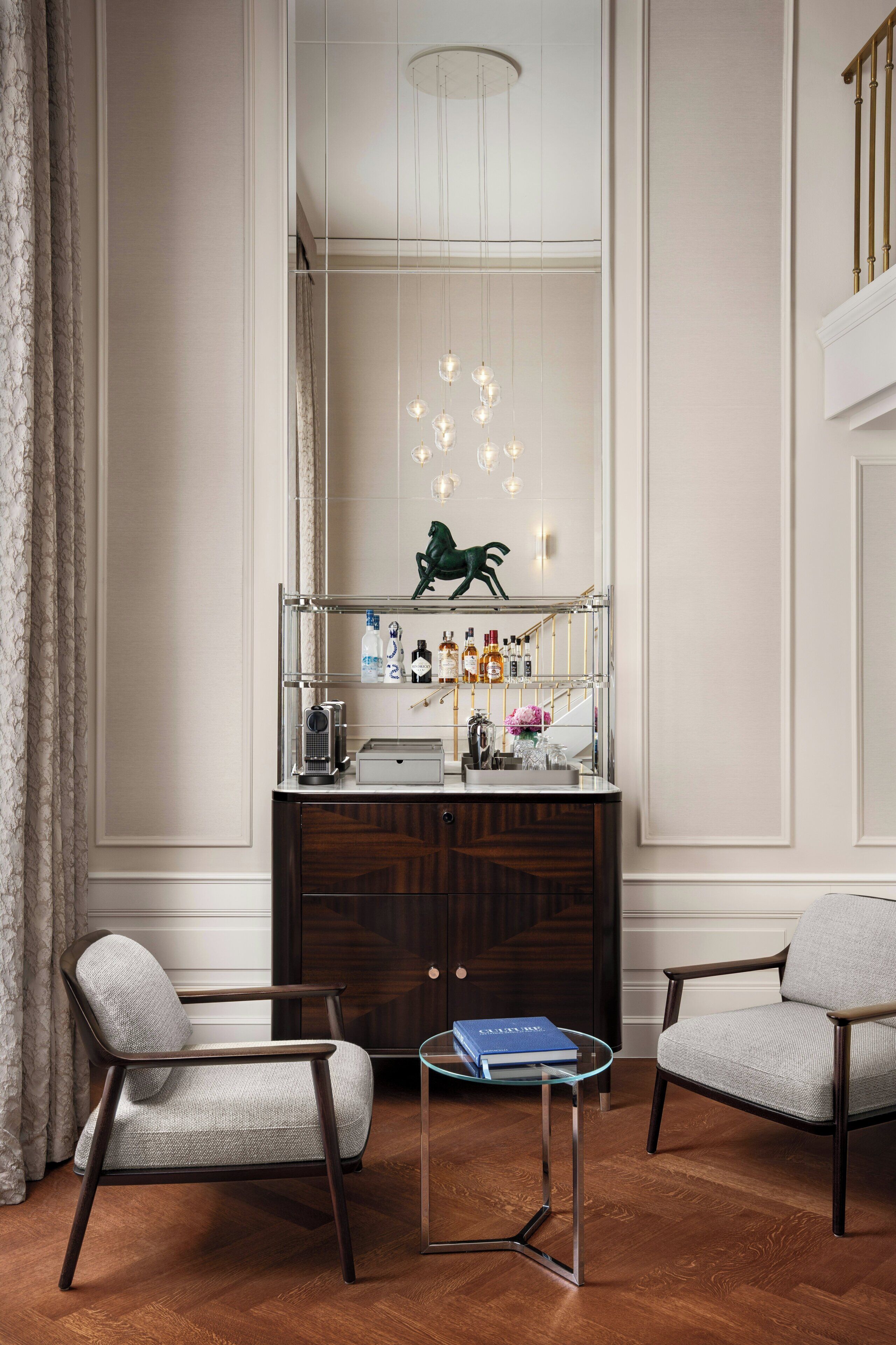 A modern interior with a wooden cabinet, two armchairs, a glass table, and a decorative mirror with a green sculpture.