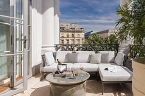 A sunlit outdoor seating area with a sofa, a round table, and a bottle of champagne. - Palais Coburg  (Vienna)