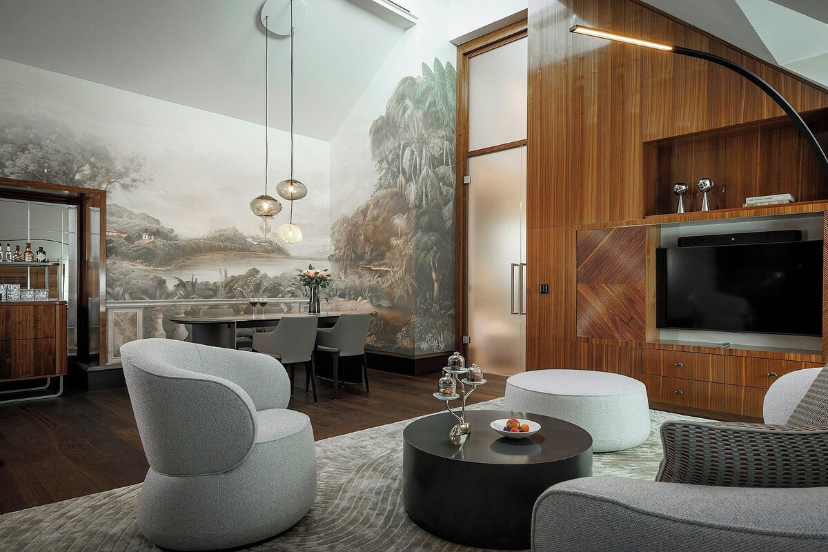 A modern living room with a large TV, comfortable seating, a dining area, and a mural on the wall.