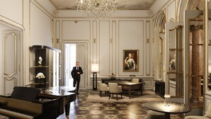 A grand room with a grand piano, a chandelier, a portrait, and a man in a suit. - Palais Coburg  (Vienna)