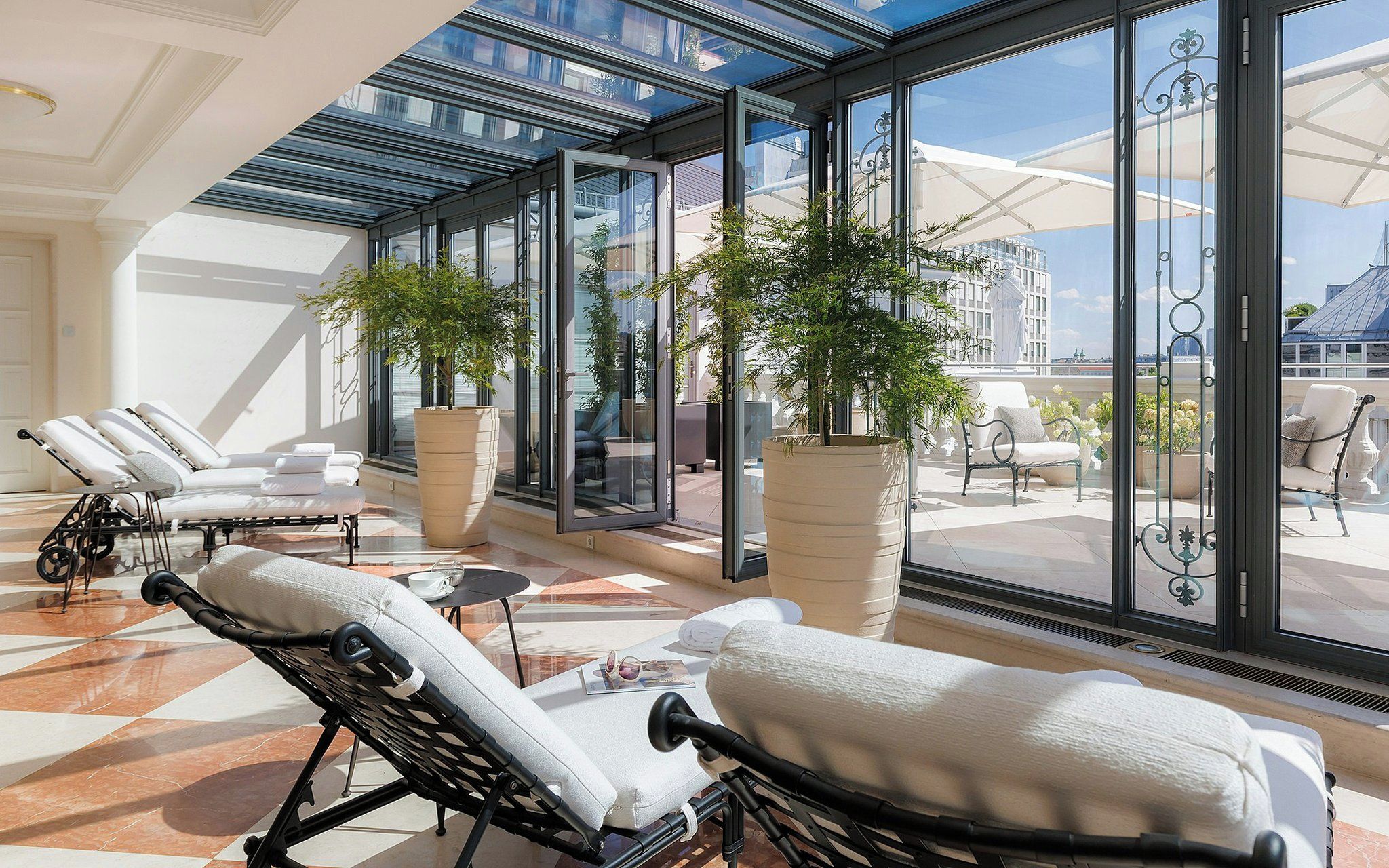 Ein sonnendurchfluteter Lounge-Bereich mit modernen Loungestühlen, üppigen Topfpflanzen und Blick auf die Skyline durch große Glaswände.