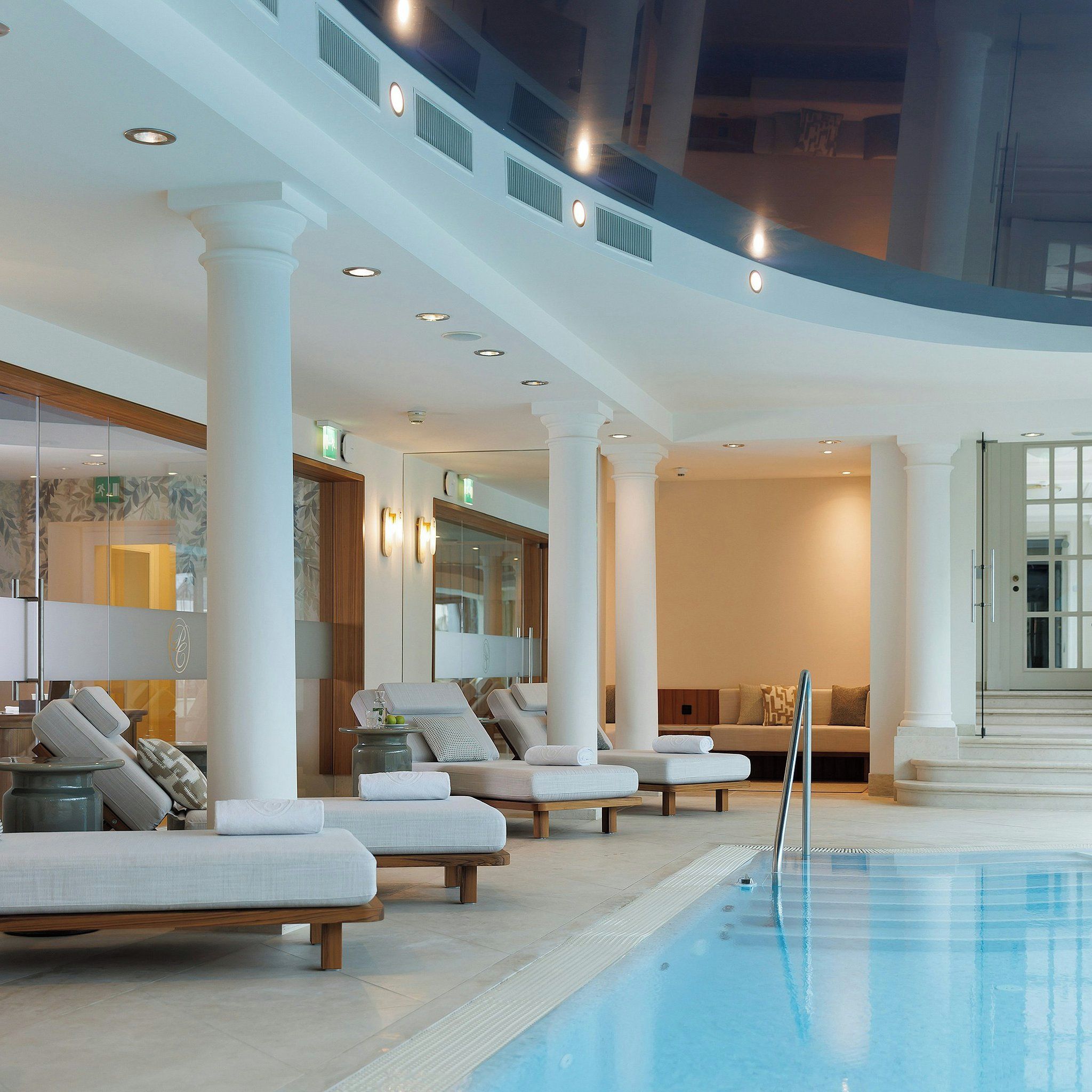 Un área de piscina con sillones de descanso y una zona de estar con paredes de vidrio.