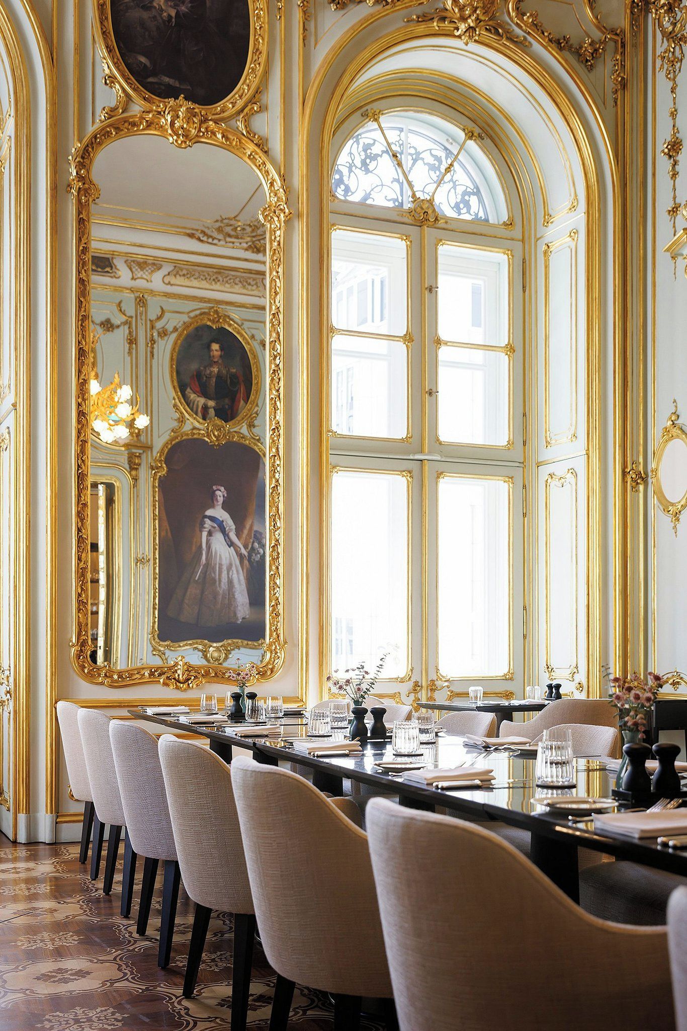 Une salle à manger élégante, avec une longue table, des chaises et des miroirs décoratifs encadrés d’or.
