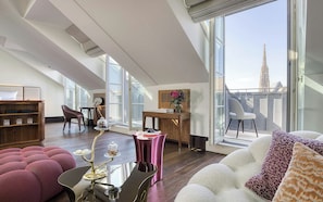 A spacious living room with a large window, a wooden bookshelf, a dining table with a vase, and a sofa with patterned cushions. - Palais Coburg  (Vienna)