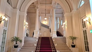 A grand staircase with a red carpet, flanked by columns and potted plants, leading to an upper level. - Palais Coburg  (Vienna)