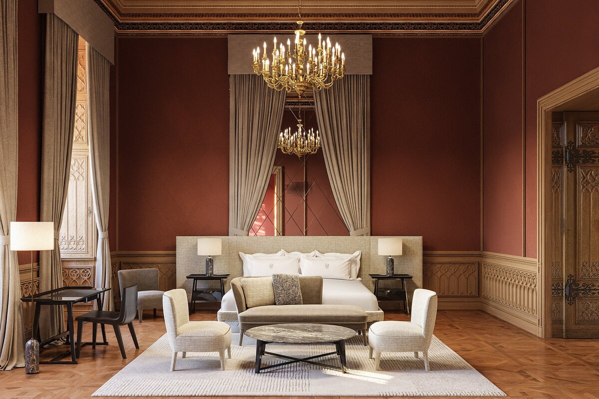 A luxurious bedroom with a large bed, two armchairs, a coffee table, a chandelier, and a large window with curtains.