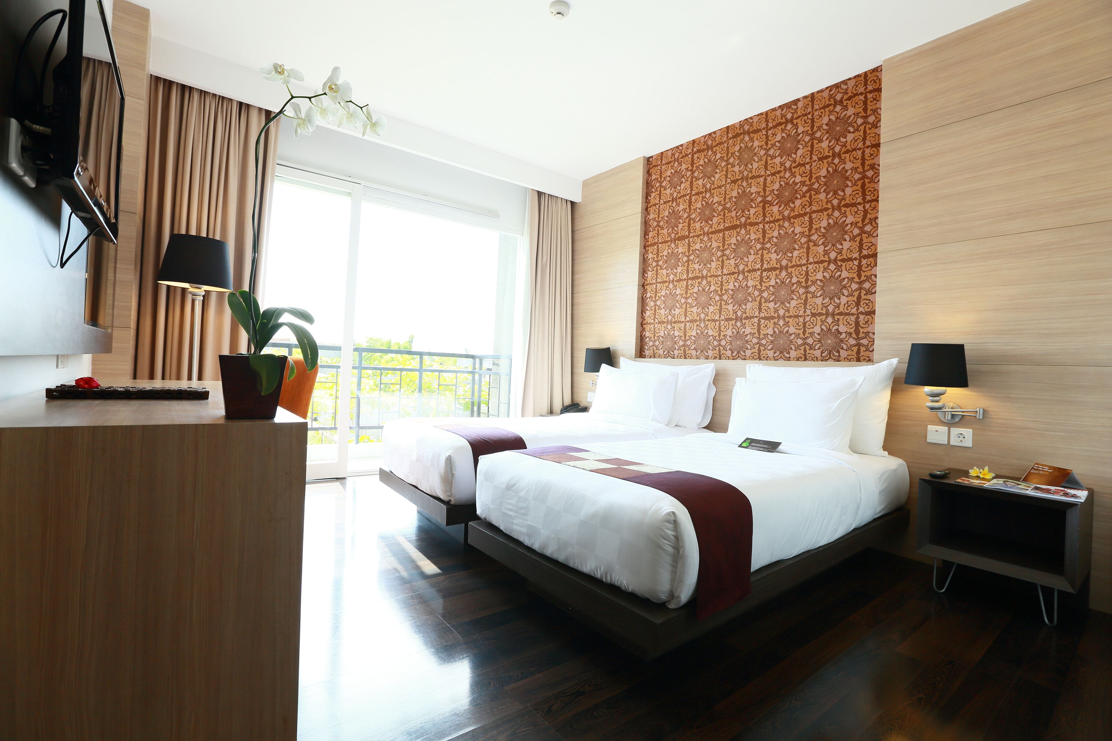 A modern hotel room with a large bed, a desk, a potted plant, and a view of the outdoors.