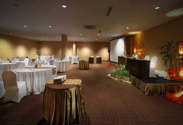 Un salón de conferencias con mesas redondas, sillas, un escenario y una pantalla.