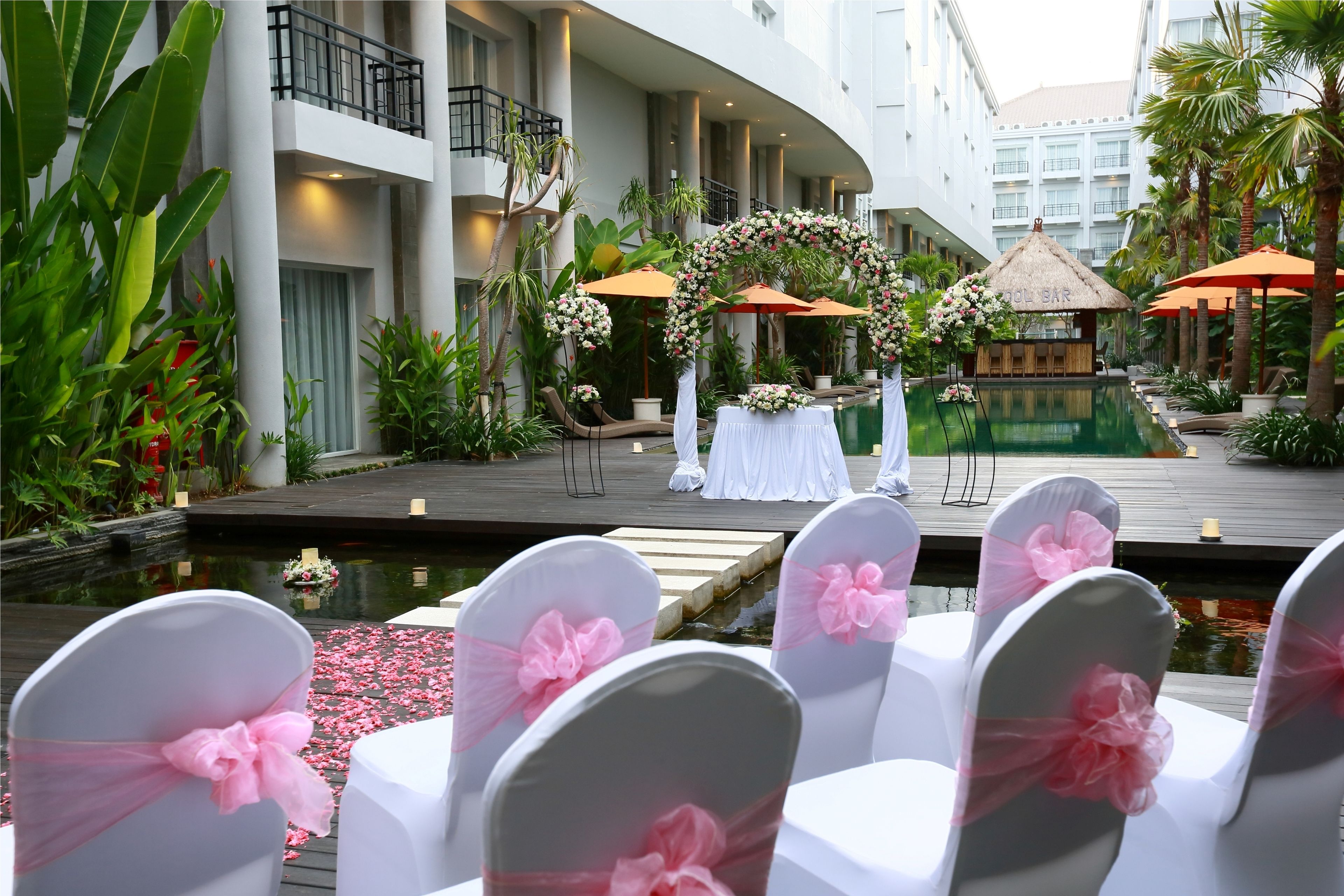 A wedding ceremony setup with a stage, floral decorations, and a poolside seating area.