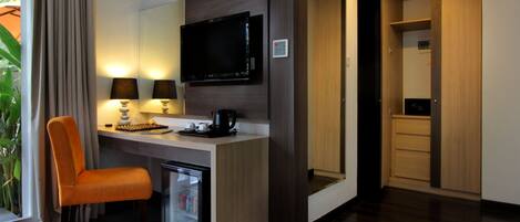A modern hotel room with a desk, chair, flat-screen TV, and built-in storage.