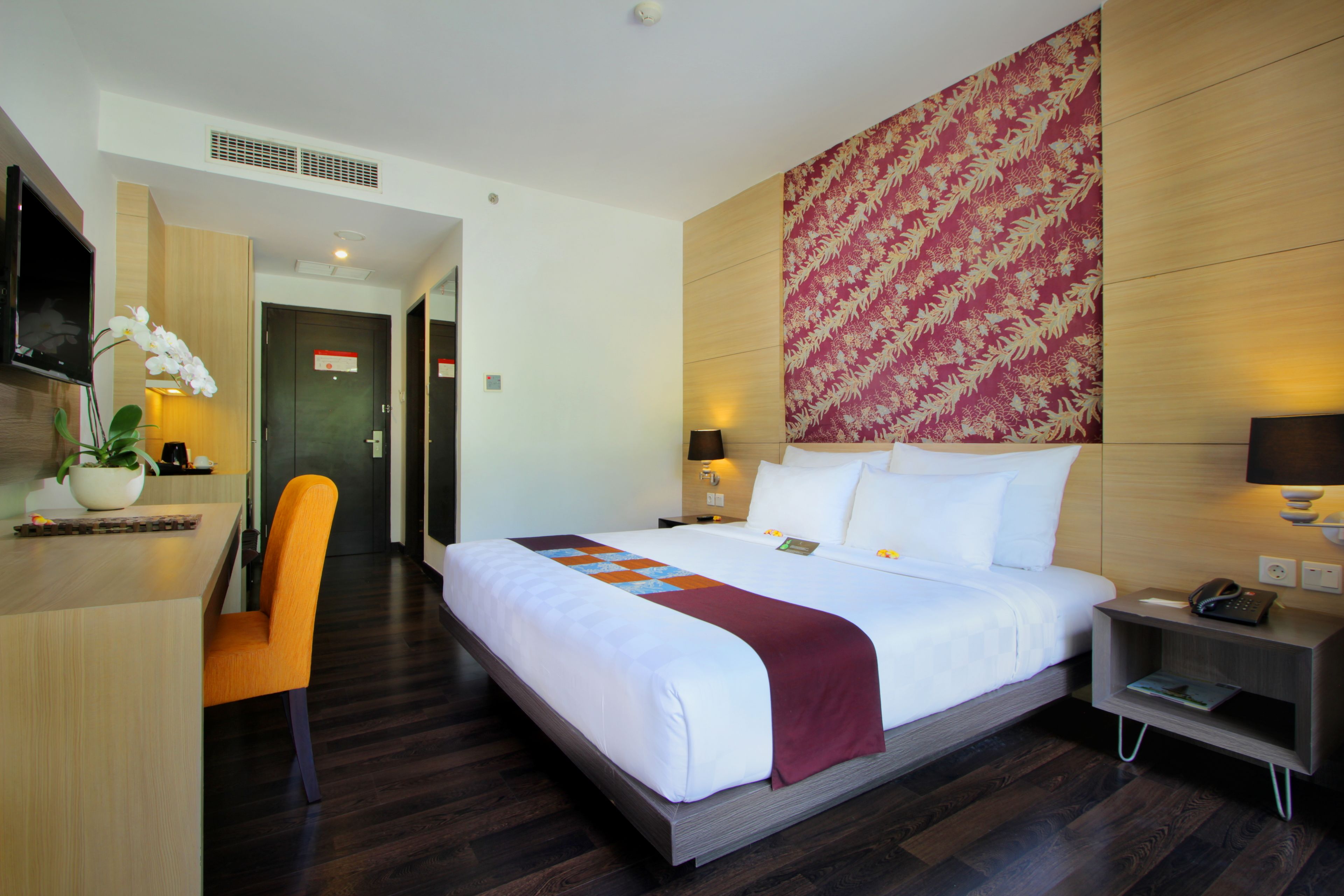 A hotel room with a large bed, a desk with a chair, a TV, and a wall-mounted artwork.