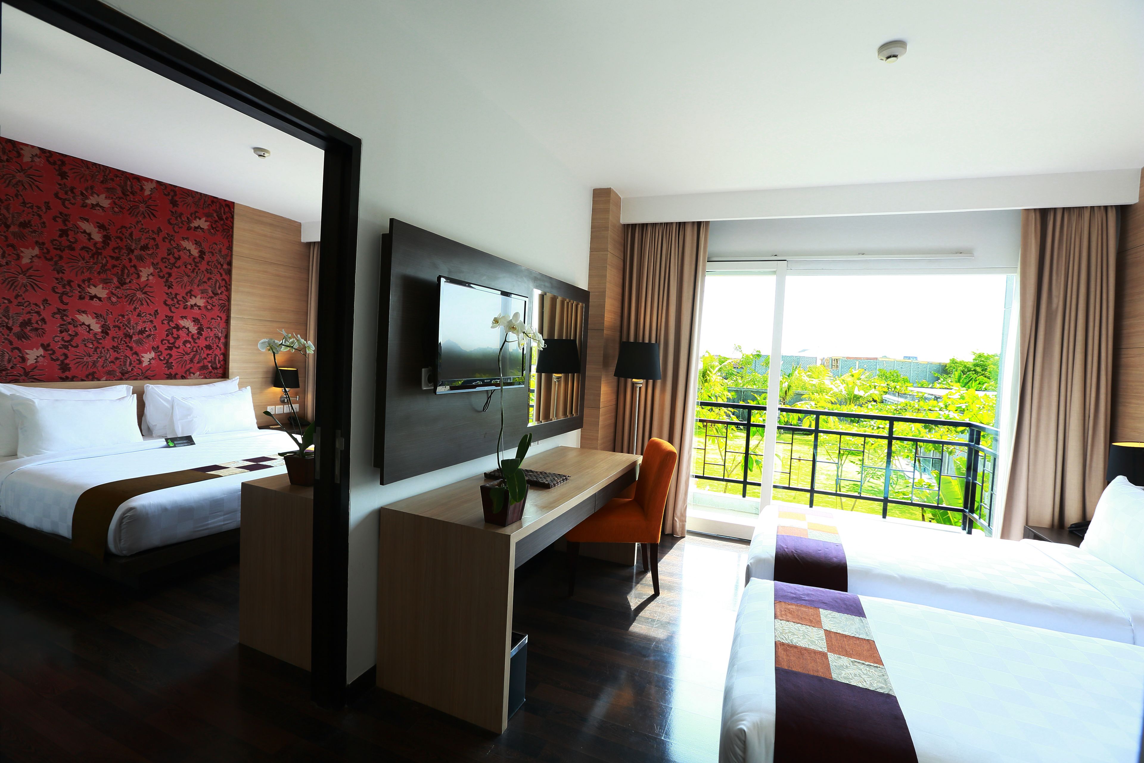 Habitación de hotel con cama, escritorio, televisión y balcón con vistas.