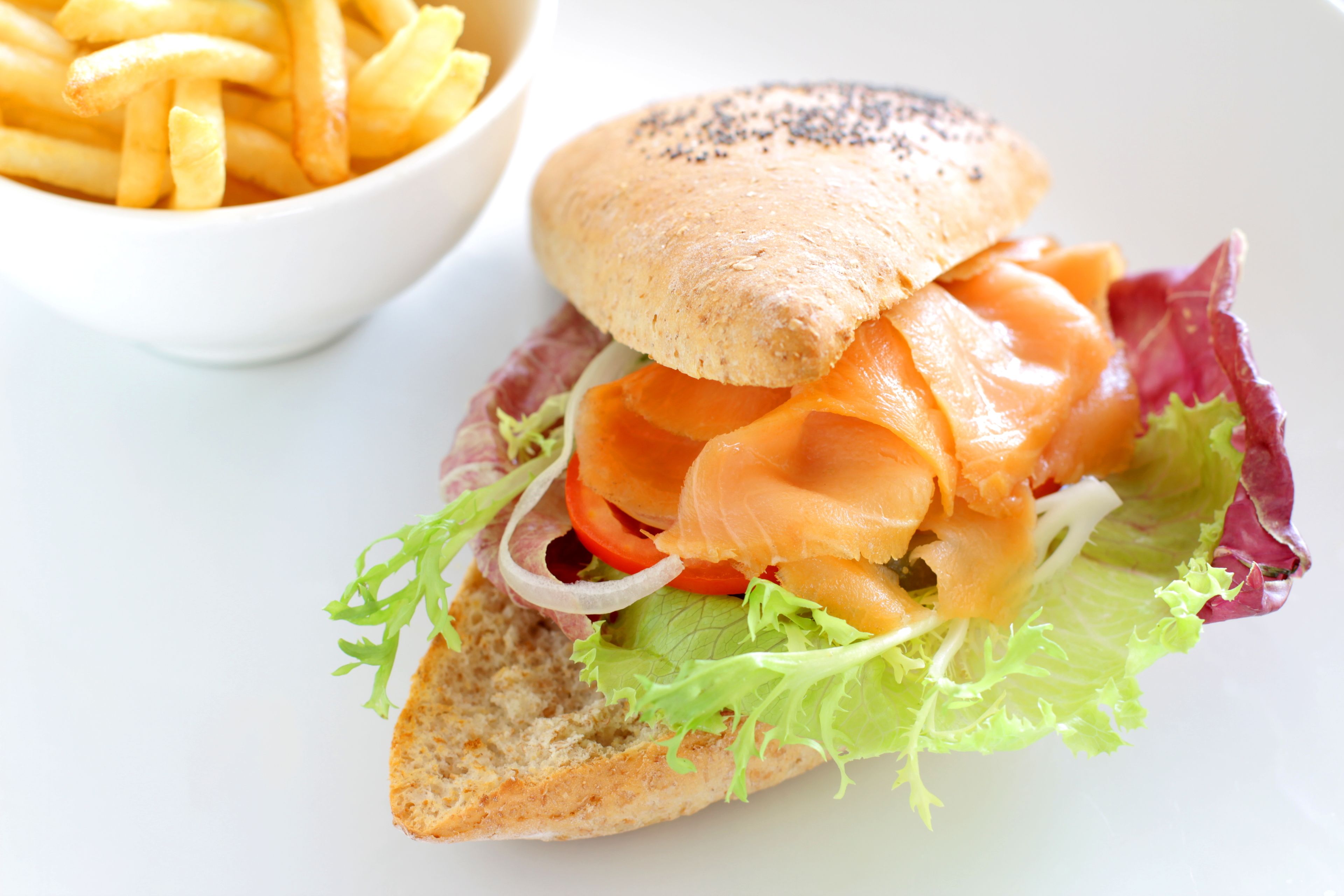 Un sándwich de pan con lechuga, tomate y salmón ahumado, acompañado de una porción de papas fritas.