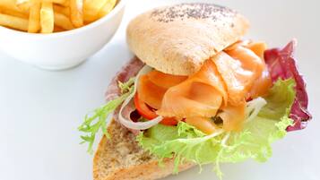 Un sándwich de pan con lechuga, tomate y salmón ahumado, acompañado de una porción de papas fritas.