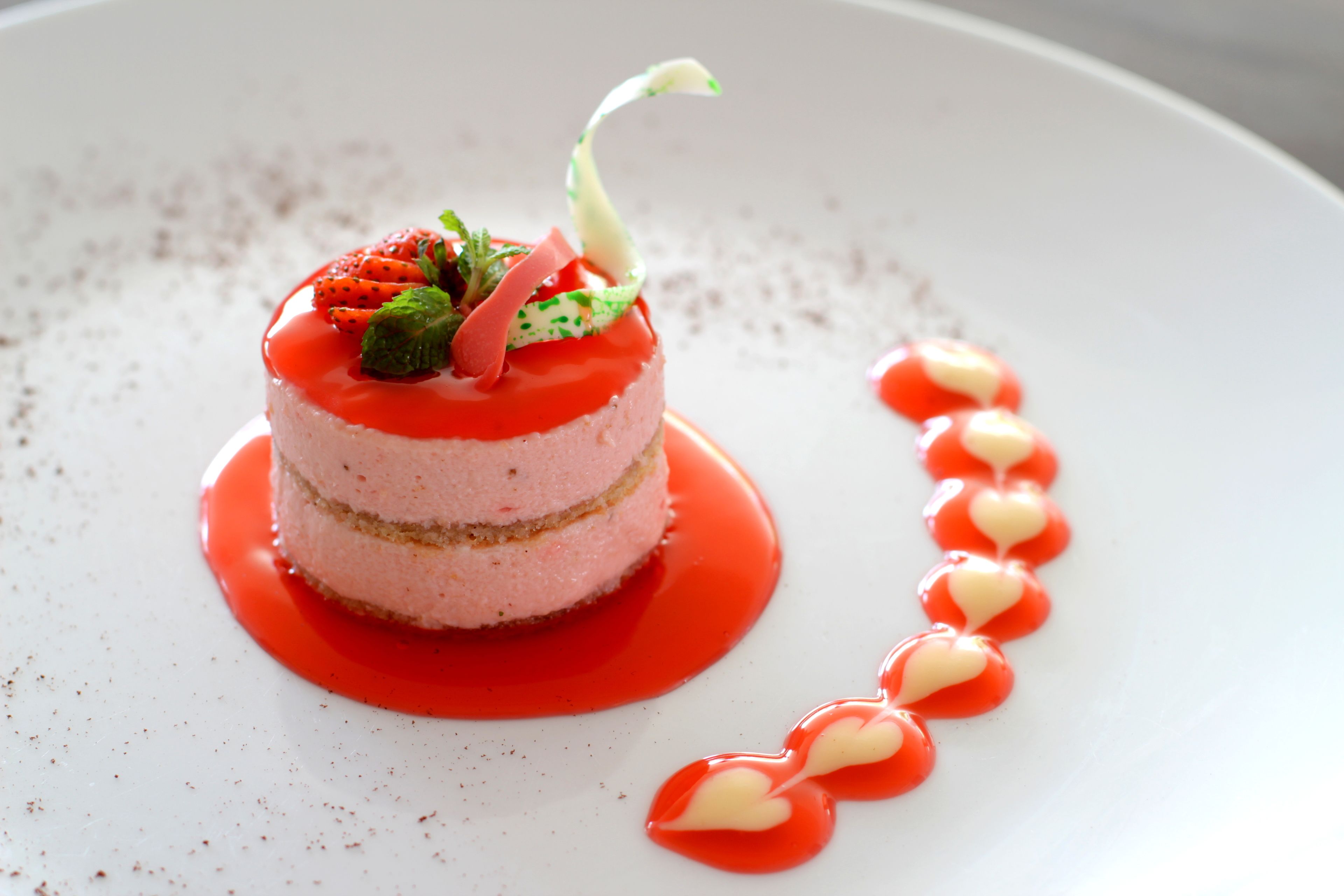 A dessert on a white plate with a red sauce and heart-shaped decorations.