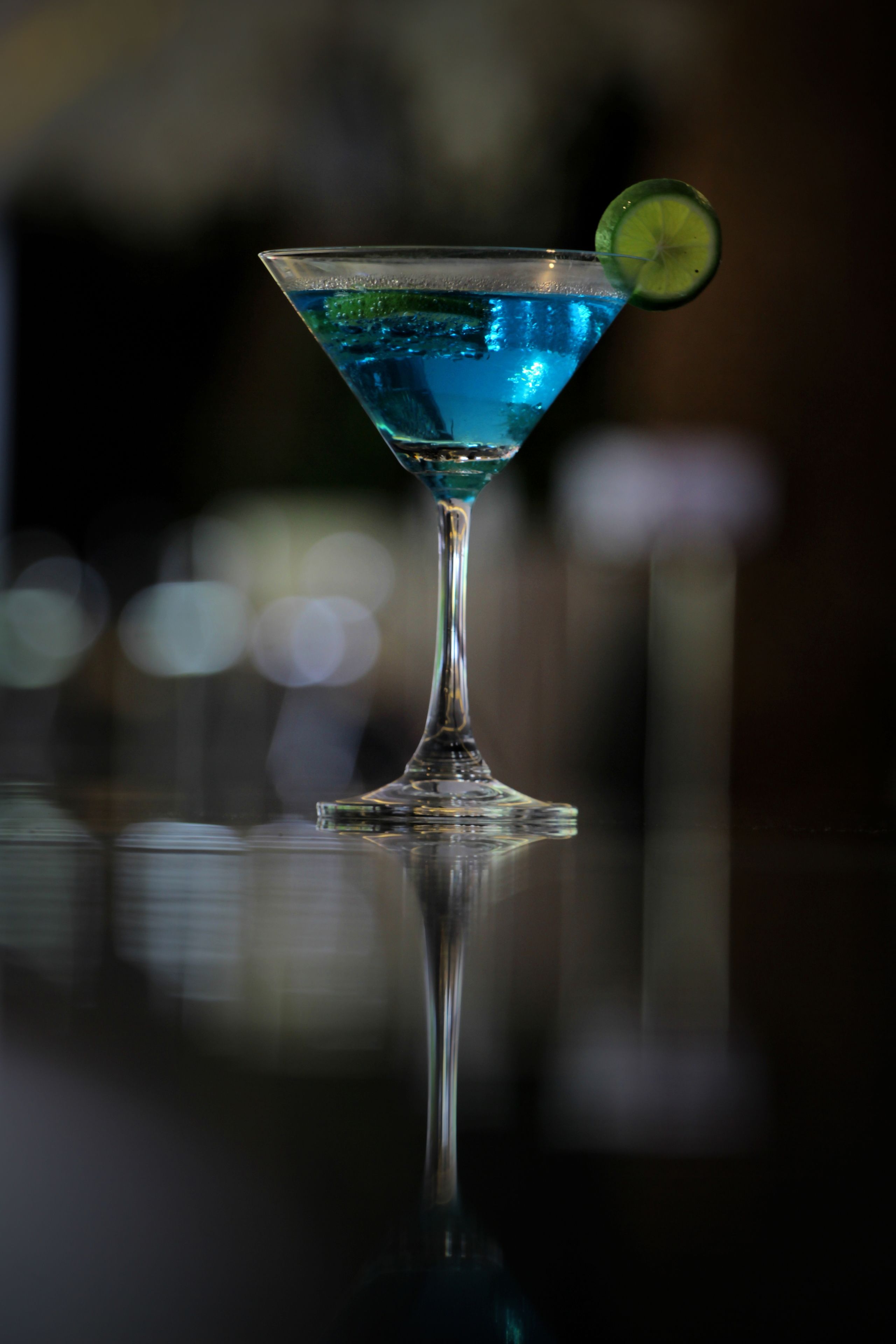 Een martini glas met een limoen schijfje op een reflecterend oppervlak.