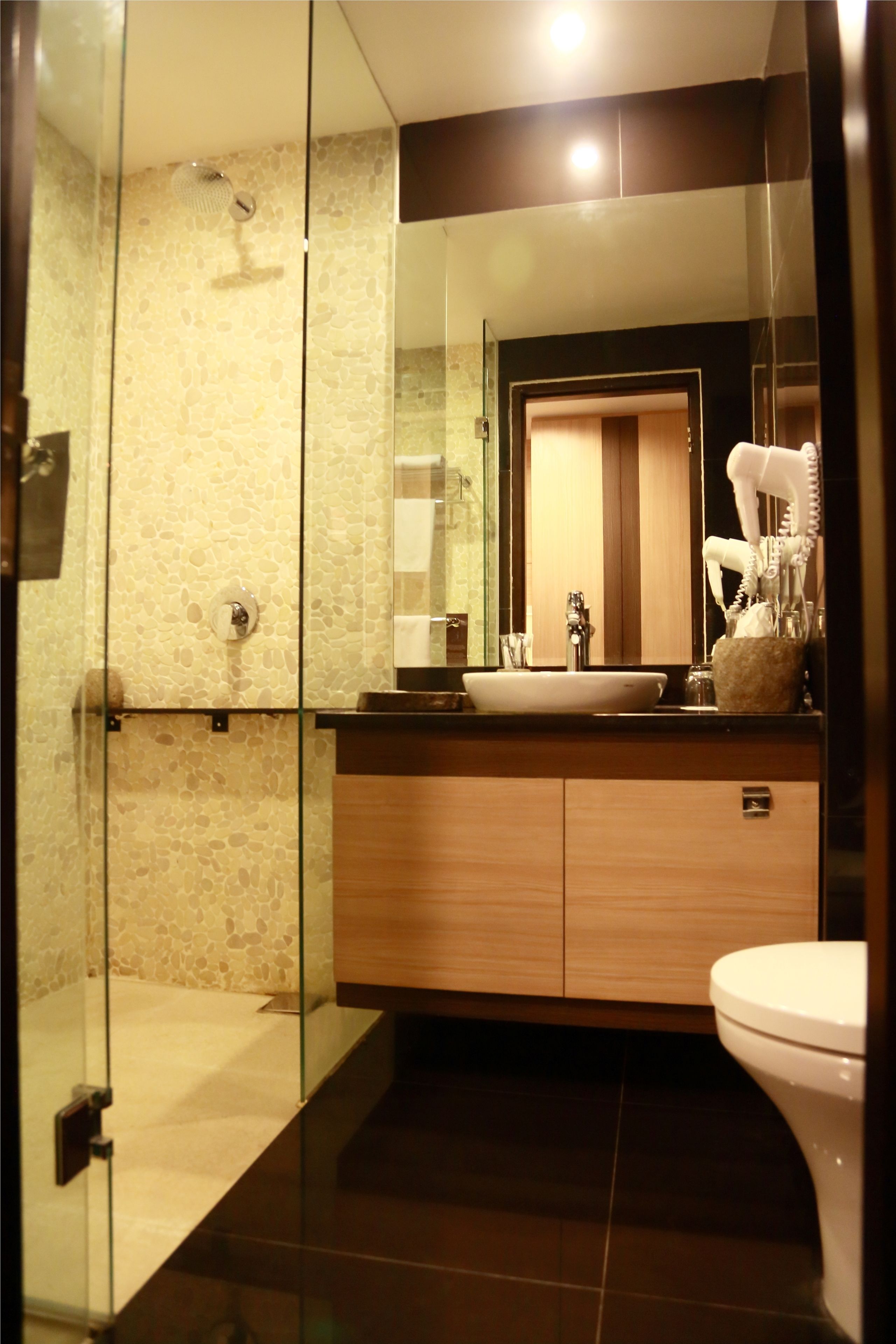 Un baño moderno con ducha envuelta en vidrio, tocador de madera con lavabo e inodoro.