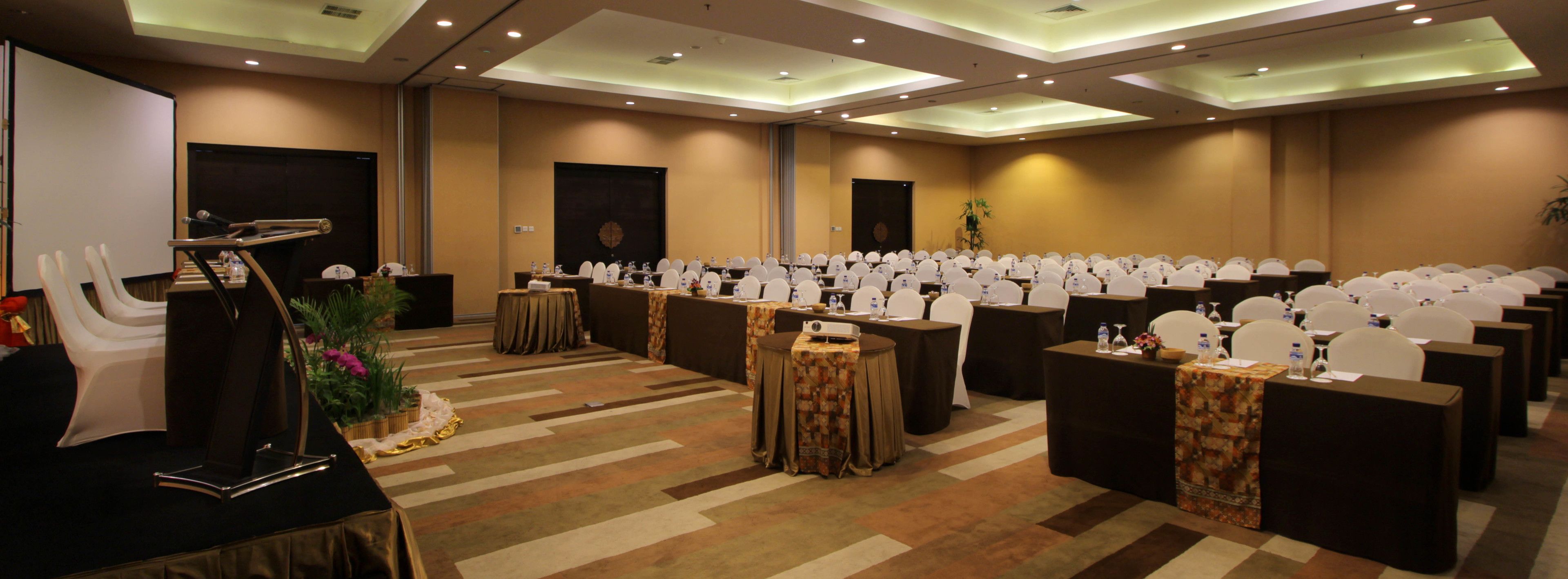 A conference room with rows of tables and chairs, a podium, and a projector screen.