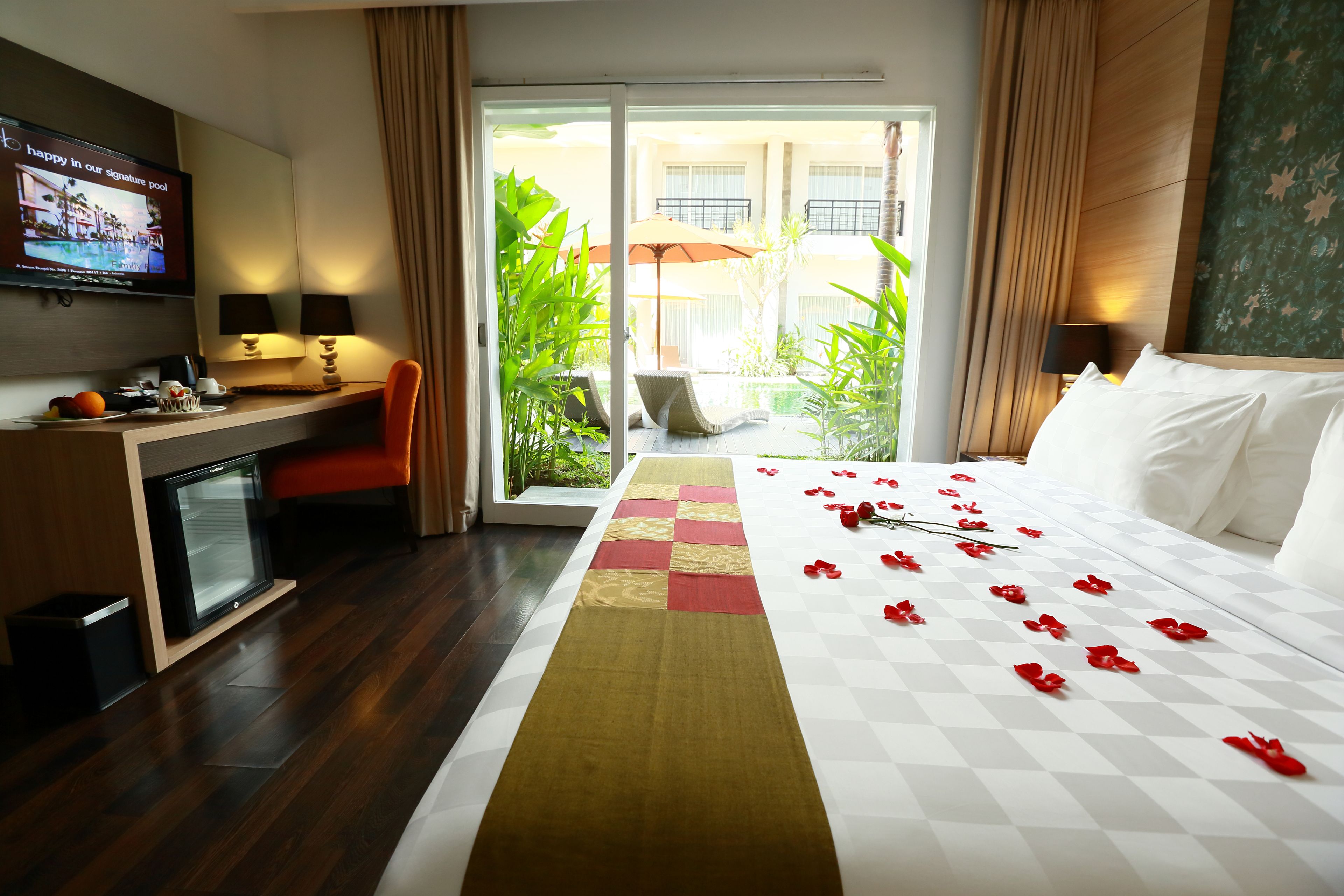 A hotel room with a bed, a desk, a television, and a view of the outdoor area.