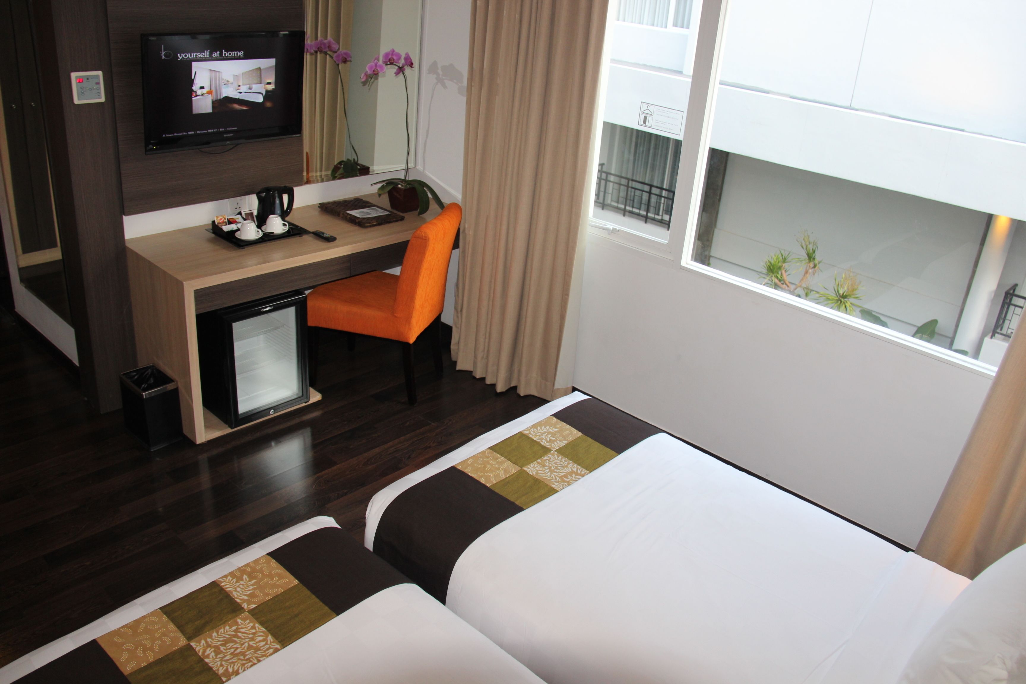A hotel room with a bed, a desk with a computer, a chair, a TV, and a window with a view of the outside.