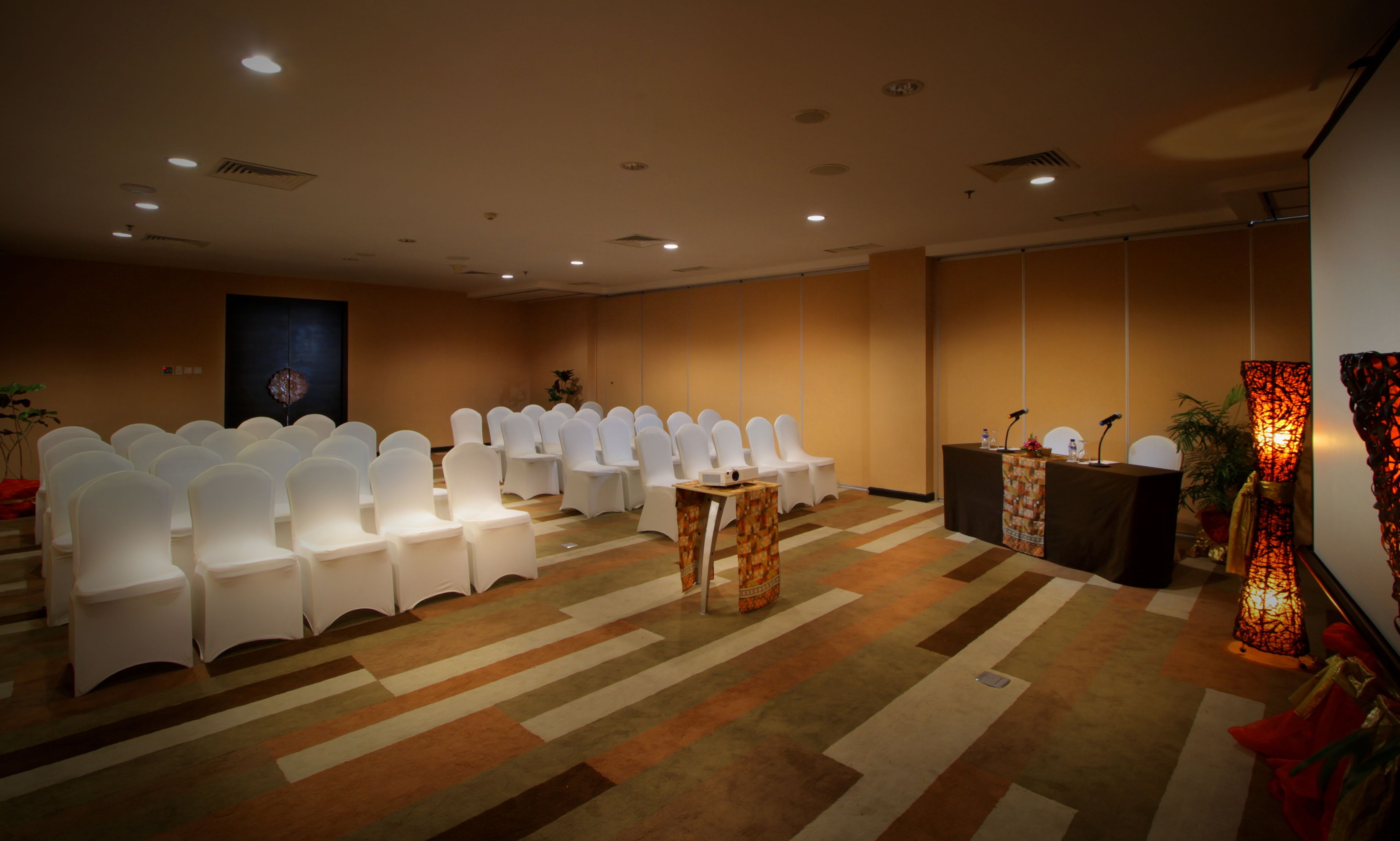 A conference room with rows of white chairs, a podium with microphones, and a carpeted floor.