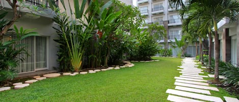 Un patio con un sendero de piedra, abundante vegetación y edificios modernos con balcones.