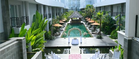 A pool area with a thatched gazebo, white chairs, and a flower-decorated walkway.
