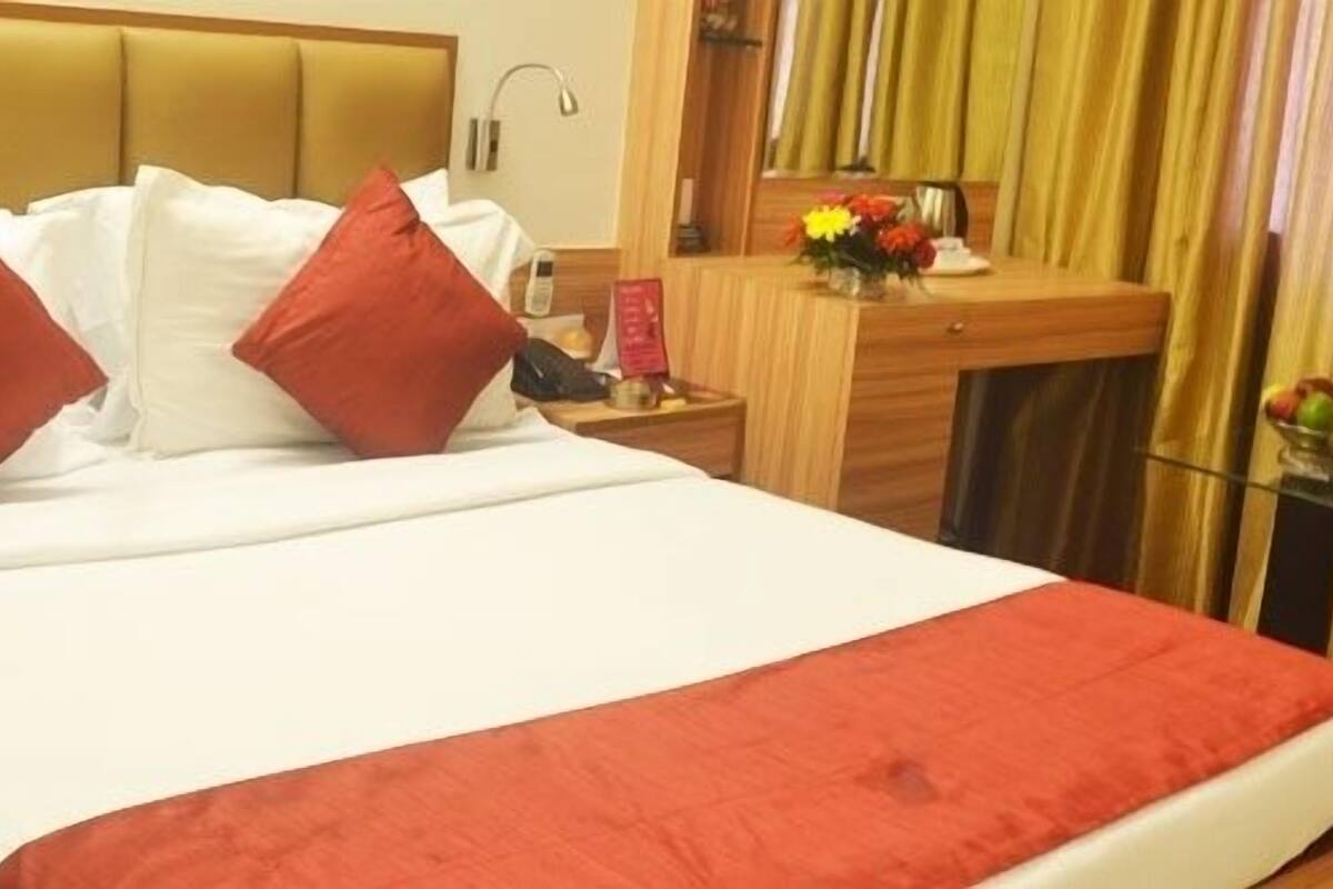 A hotel room with a bed, a desk with a chair, a telephone, and a small table with fruit.