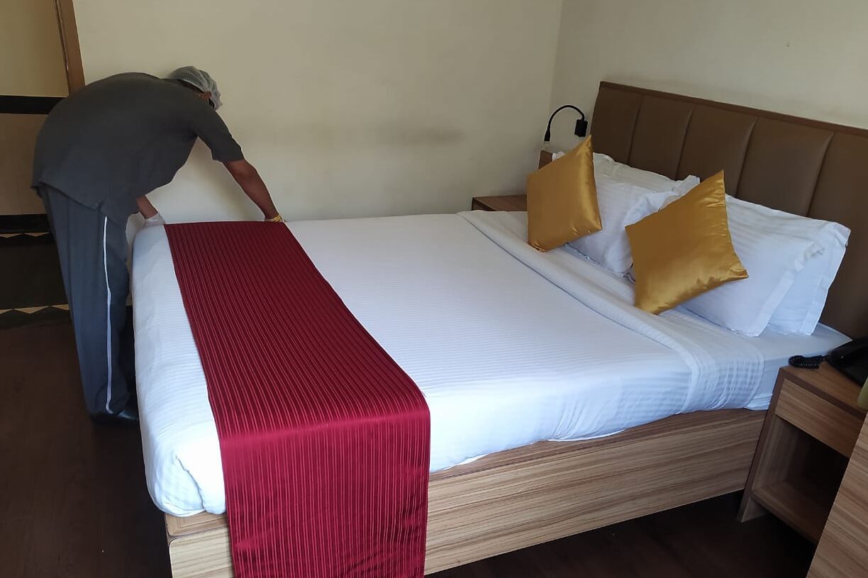 Ein ordentlich gemachtes Bett mit roter Bettdecke und zwei goldenen Kissen, ein Holzkopfende und ein Nachttisch mit Lampe.