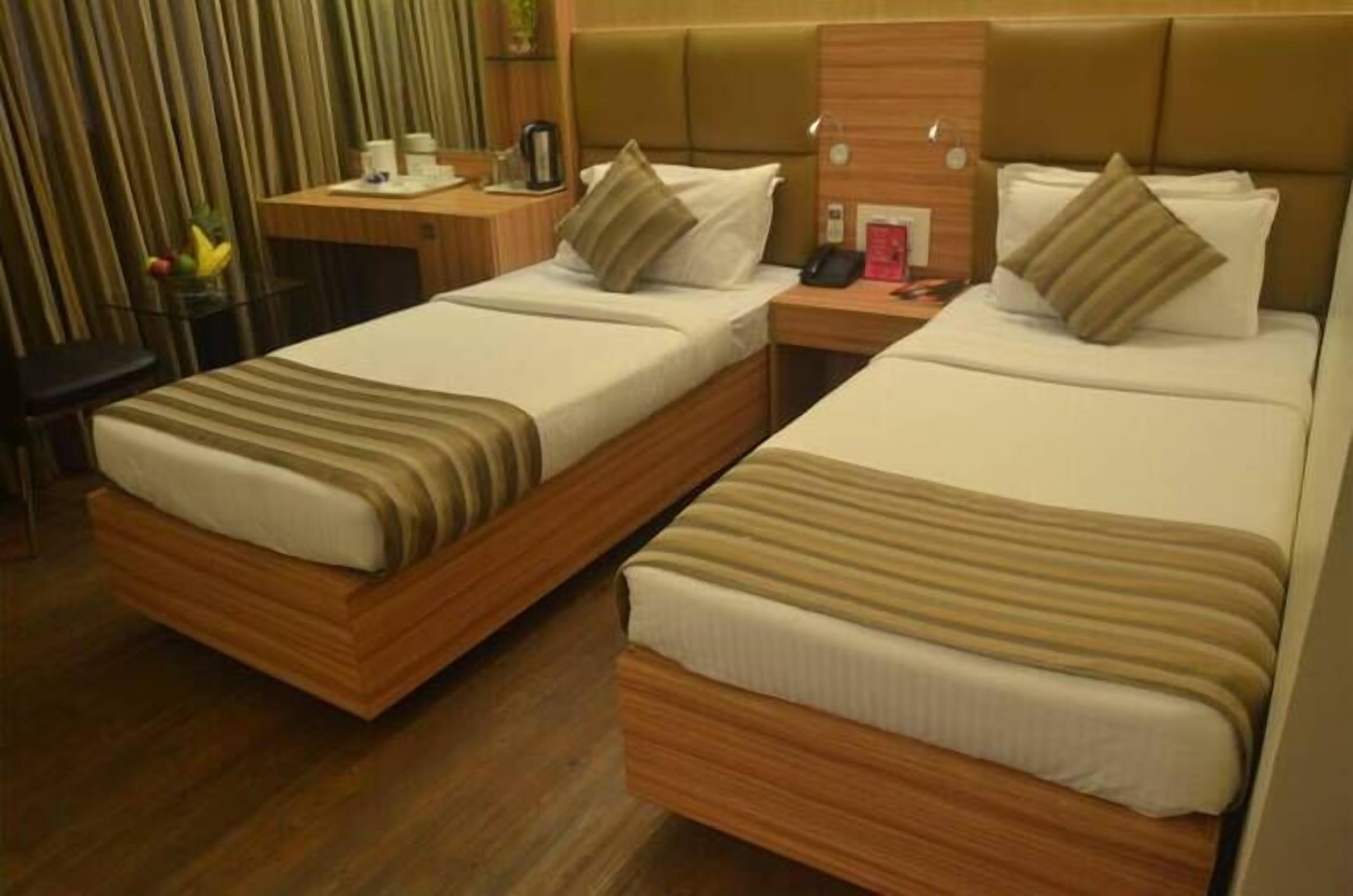 Ein Hotelzimmer mit zwei Einzelbetten, Holz-Kopfteilen, einem kleinen Schreibtisch mit Stuhl sowie einem Nachttisch mit Telefon und Lampe.