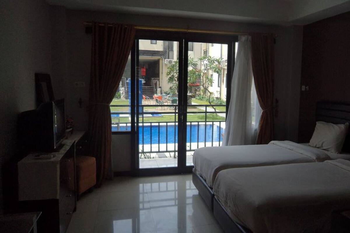 A hotel room with two beds, a TV, and a view of a swimming pool.