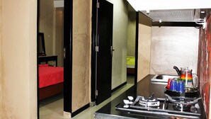 Une chambre d’hôtel compacte, dotée d’une kitchenette, d’un lit recouvert d’une couverture rouge et d’une porte donnant sur une autre pièce.