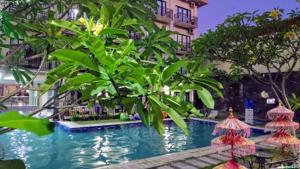 Un espace piscine agrémenté d’un grand arbre, de chaises longues et de parasols.