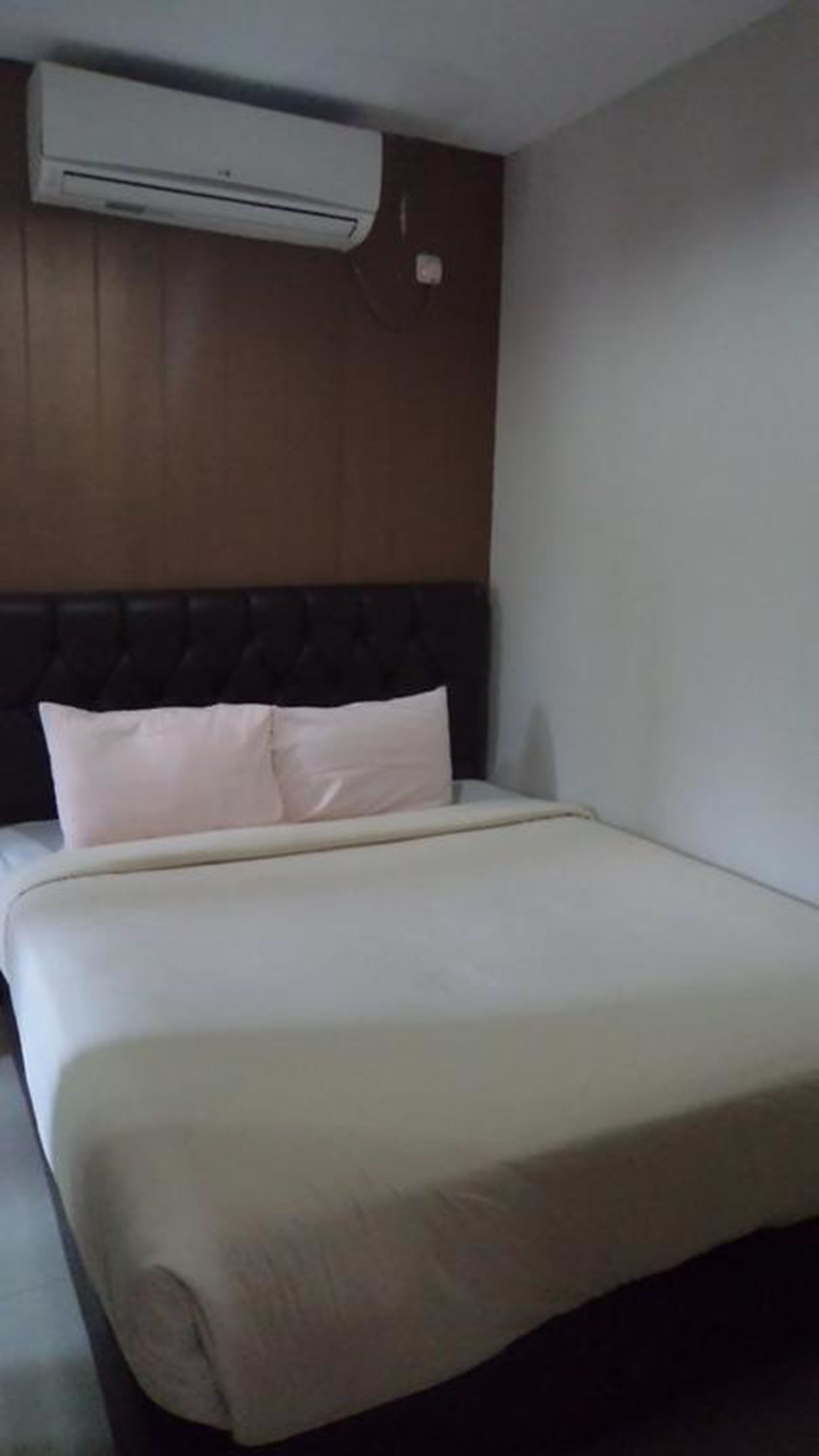 A hotel room with a bed, a headboard, and an air conditioning unit mounted on the wall.
