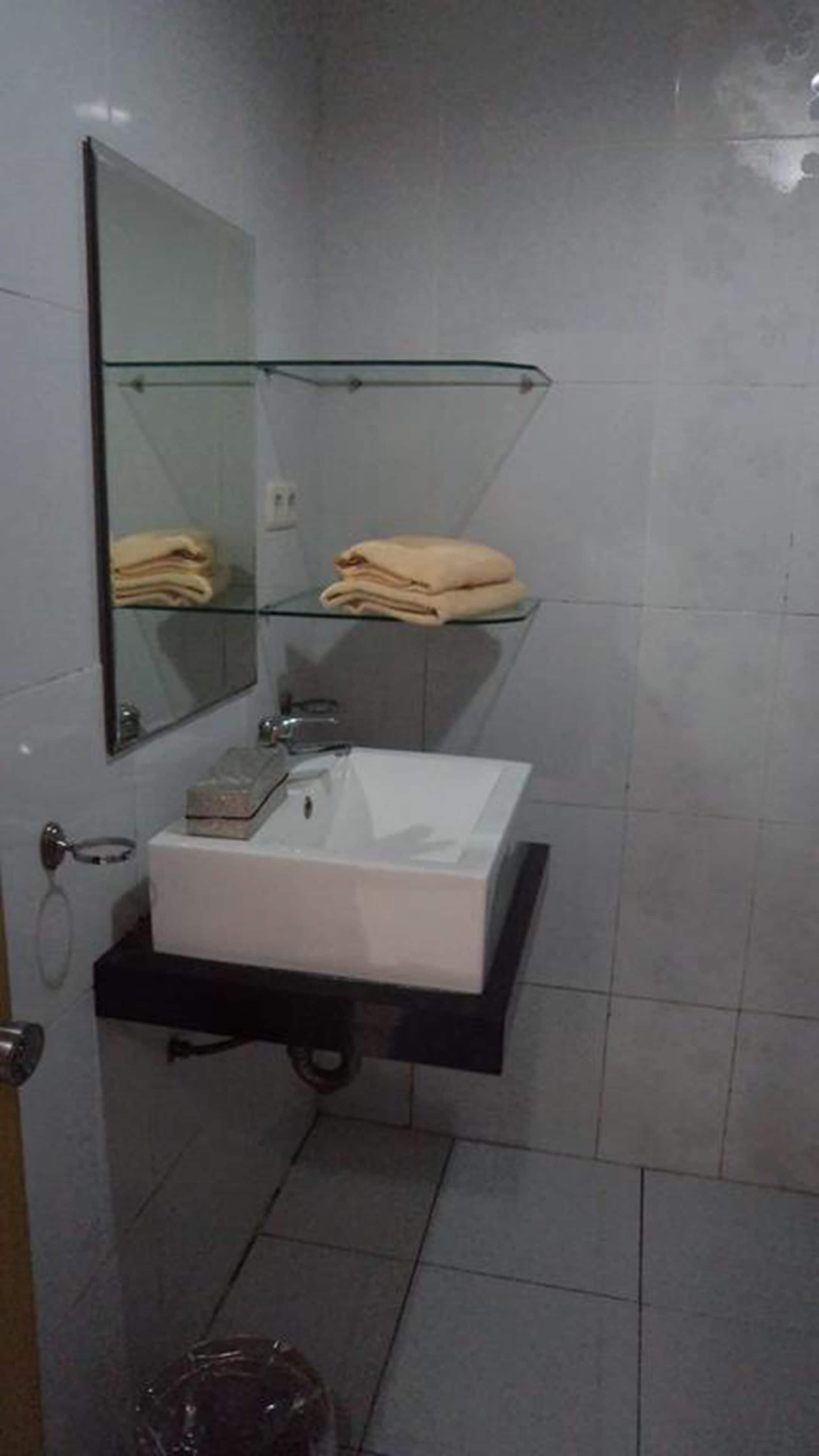 A bathroom with a white sink, a glass shelf above it, and a mirror.