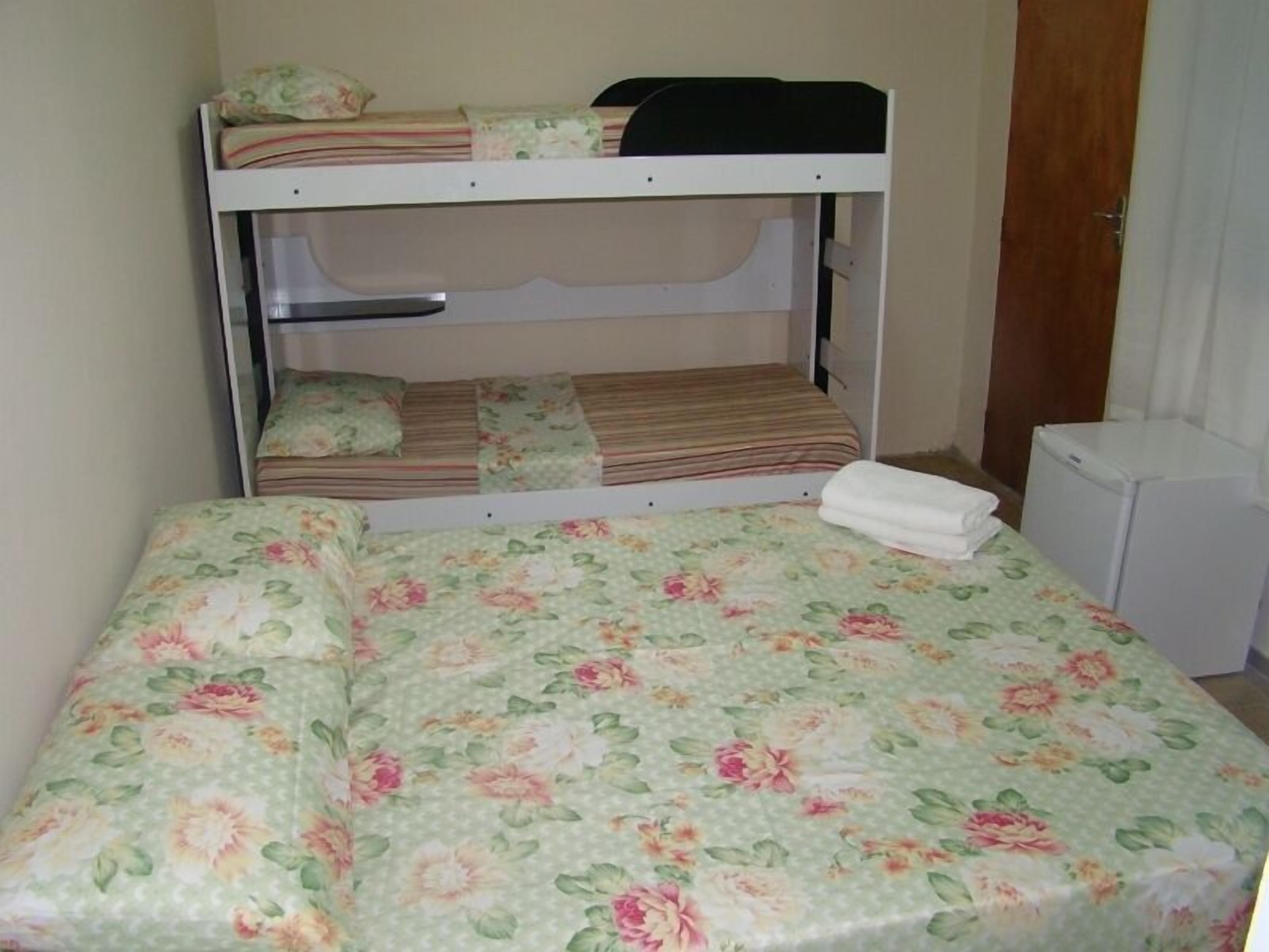 Ein Stockbett mit unterem Etagenbett und Einzelbett, beide mit Blumenmuster-Bettwäsche. Ein kleines, weißes Gerät ist rechts sichtbar.