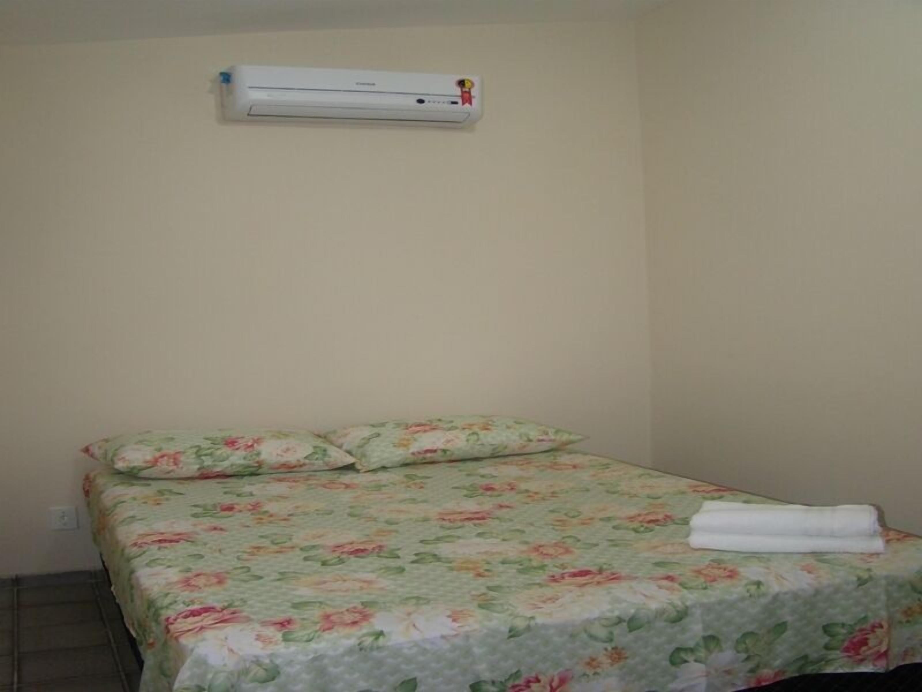 A small, simple room with a bed, a wall-mounted air conditioner, and a plain wall.
